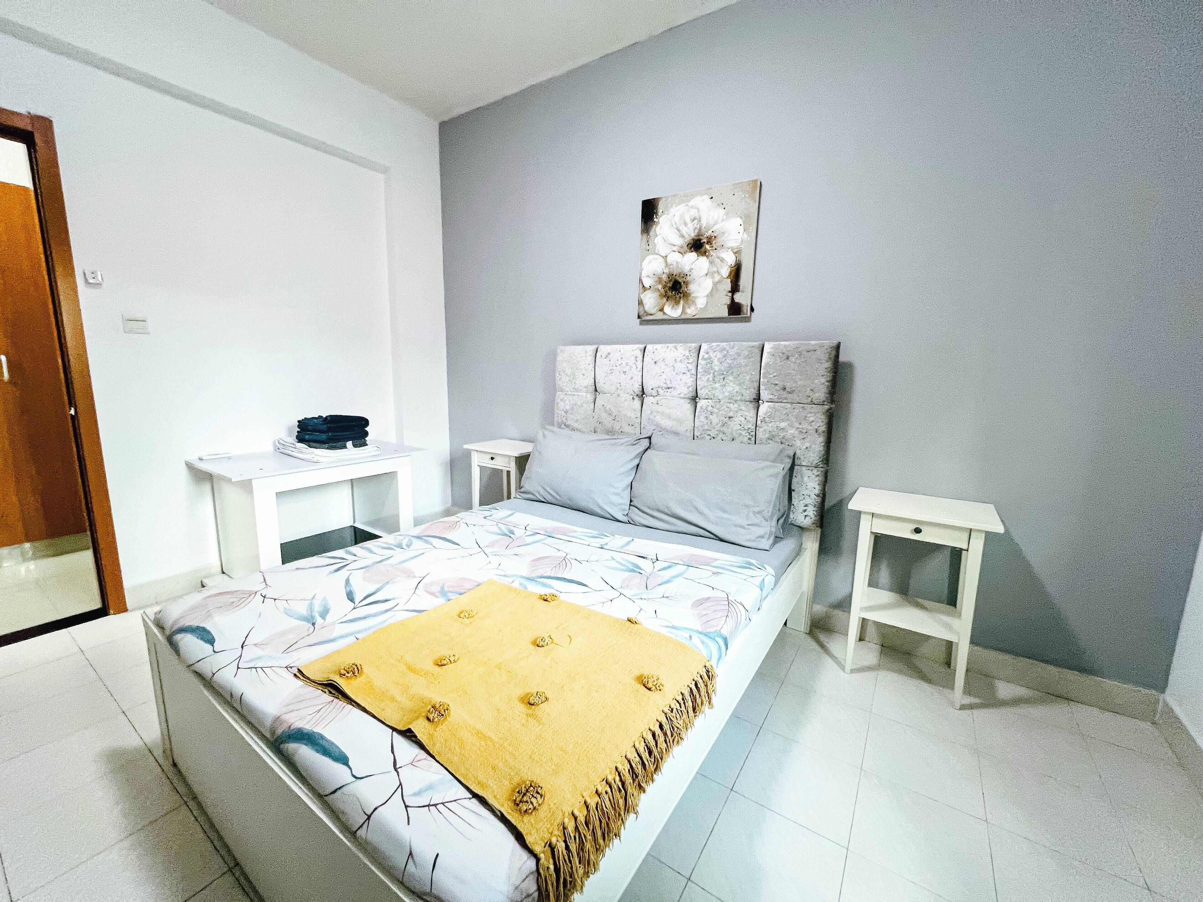 A bedroom with a bed, two bedside tables, a nightstand, a decorative wall piece, and a door.