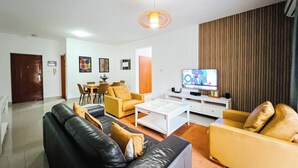 A living room with a black leather sofa, yellow armchairs, a coffee table, and a television. - 3 Bed Apartment - Sleeps 6 - Free Parking (Luanda)