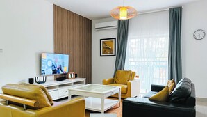 A modern living room with a television, a coffee table, two sofas, and a large window with curtains. - 3 Bed Apartment - Sleeps 6 - Free Parking (Luanda)