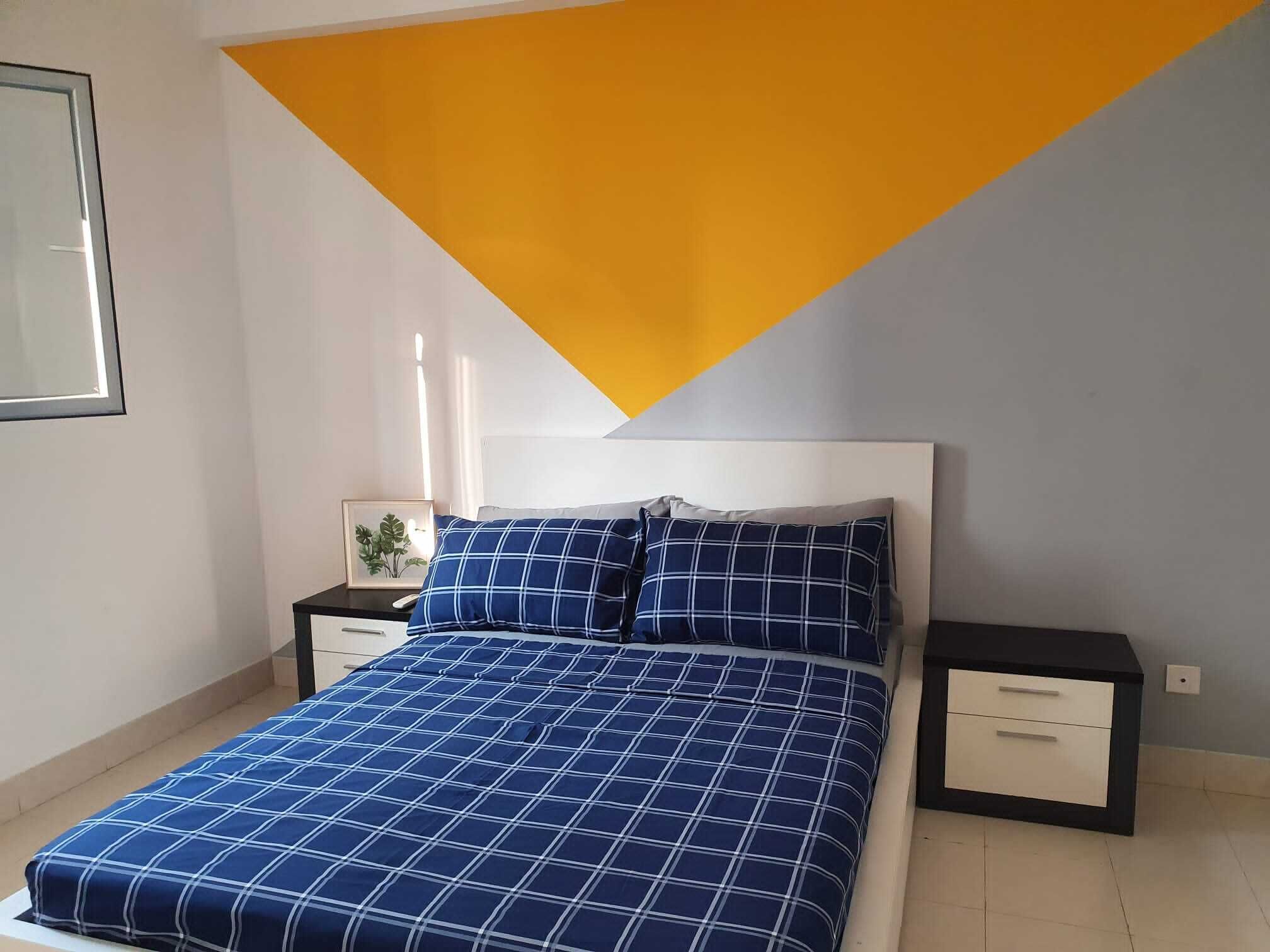 A bedroom with a bed, a nightstand, a drawer unit, and a framed picture on the wall.