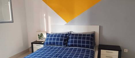 A bedroom with a bed, a nightstand, a drawer unit, and a framed picture on the wall.