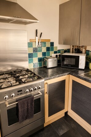 A kitchen with a gas stove, a toaster, a microwave, and wooden cabinets.