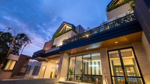 A modern hotel with a glass facade, outdoor seating, and a balcony with plants. - Valstar Hotel Canggu (Canggu)