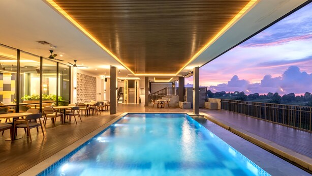 A modern indoor swimming pool with a wooden deck, glass walls, and a view of the sunset. - Valstar Hotel Canggu (Canggu)