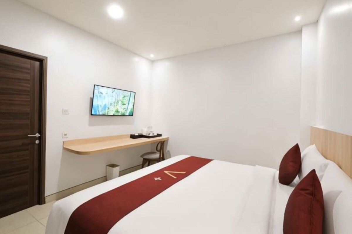 Habitación de hotel con cama, televisor montado en la pared, escritorio y cabecero de madera.