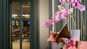 A view through a glass door into a room with chairs and tables, and a vase with pink orchids on a table. - Valstar Hotel Canggu (Canggu)
