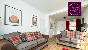 A modern living room with two grey sofas with red and grey plaid cushions, a red rug, and framed artwork on the walls.