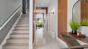 A modern hallway with a wooden staircase, a bench with a potted plant, and a wall-mounted mirror. - Fairway Prosperity: Arcade, Themed Bedroom, Golf, Private Pool, Near Disney (Kissimmee)