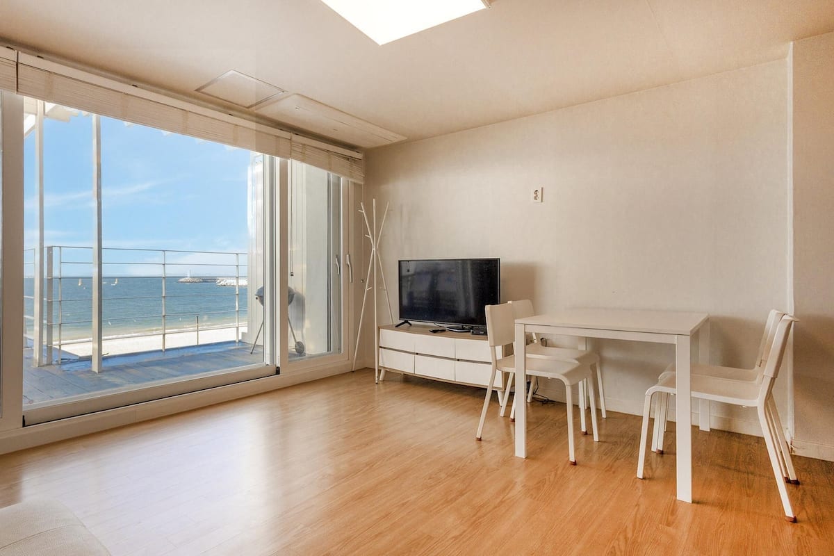 Ein geräumiges Zimmer mit einem großen Schiebeglasfenster, das auf einen Balkon mit Meerblick führt.