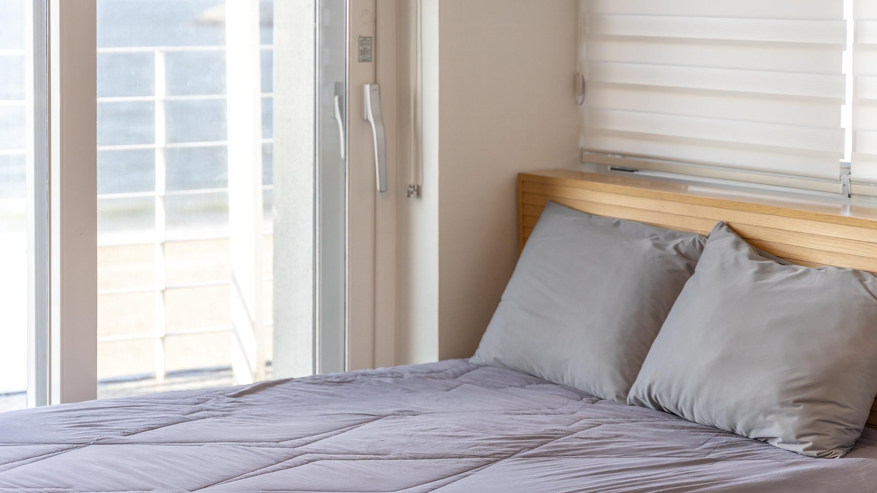 A bedroom with a bed, a wooden headboard, and a window with blinds.