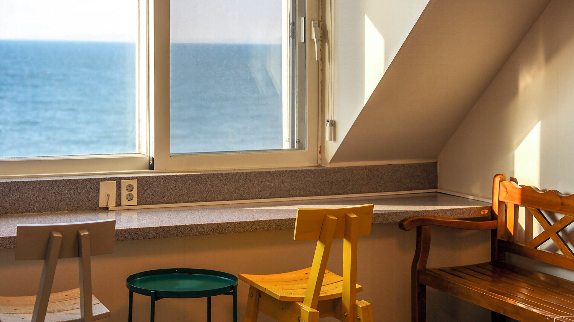 A room with a view of the sea, a window, a bench, and a chair.
