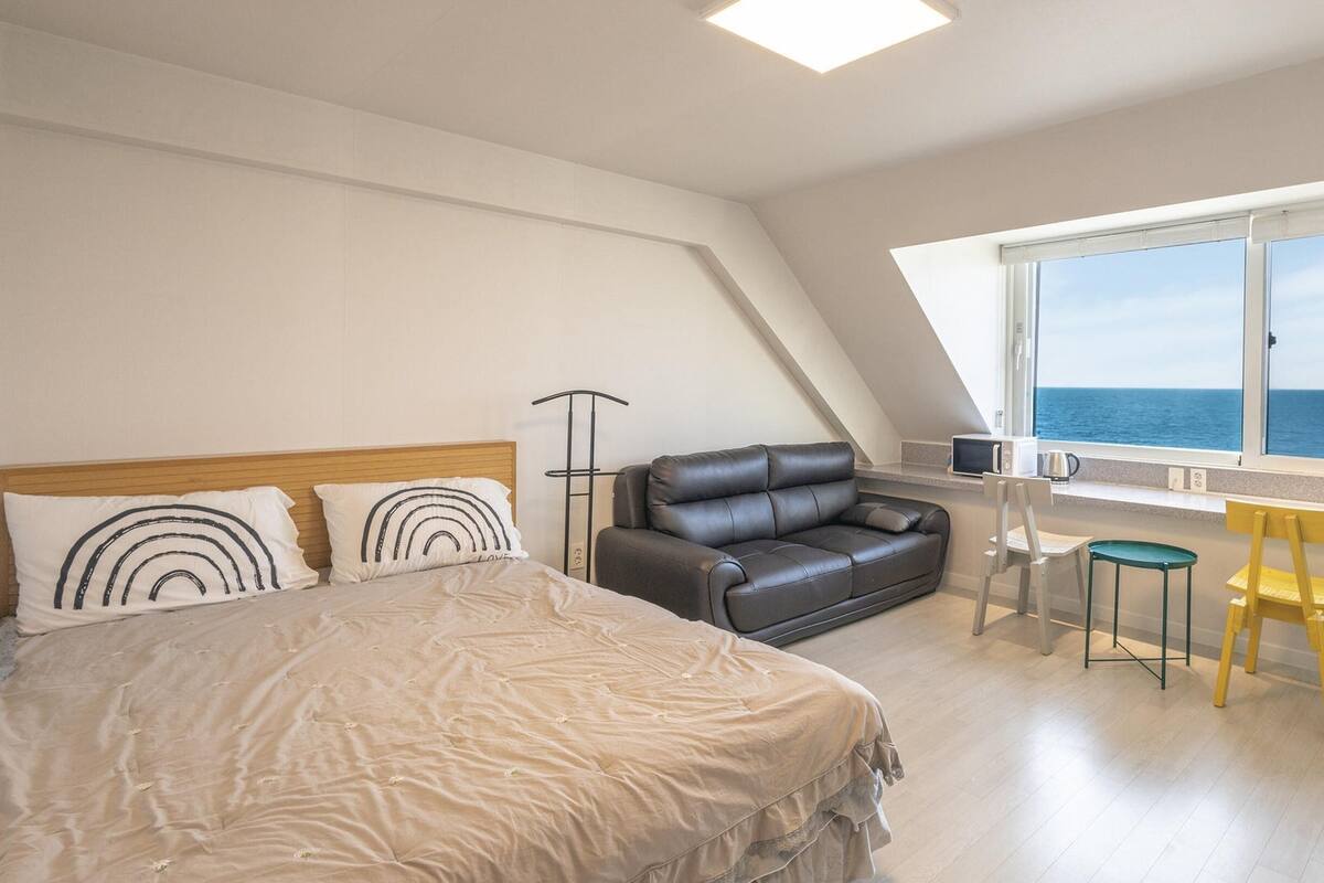 Ein Schlafzimmer mit Bett, Sofa, einem kleinen Tisch, zwei Stühlen und einem Fenster mit Meerblick.