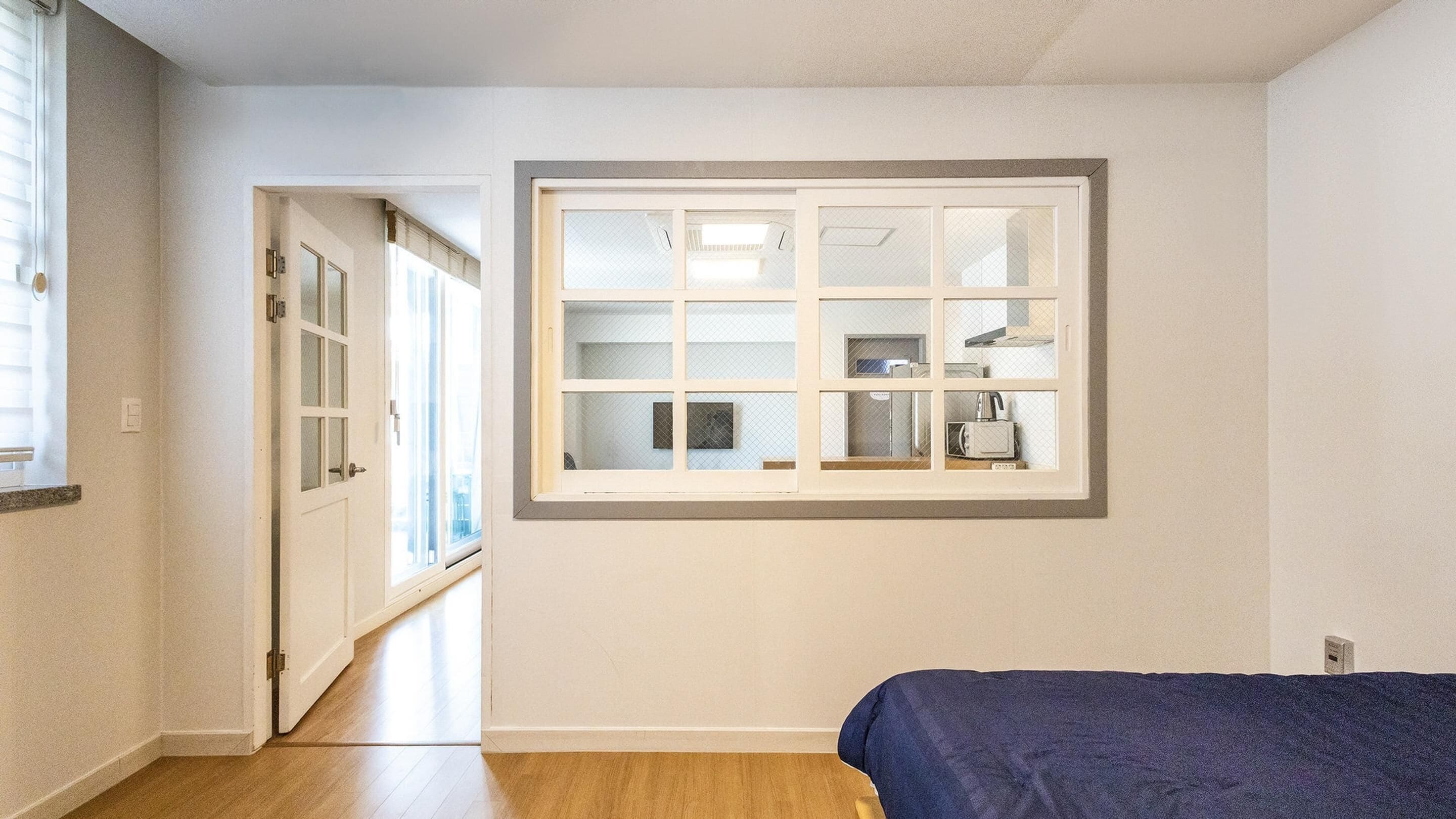 A bedroom with a large window, a bed, and a door leading to another room.