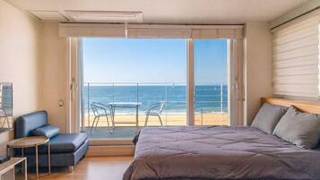 Un dormitorio con una cama grande, una mesita, un sofá y vista a la playa y al océano a través de una puerta corredera.