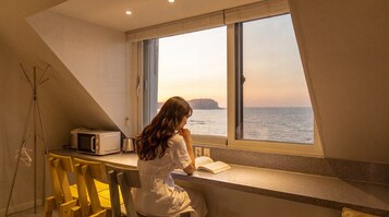 A room with a view of the sea, a window, a microwave, and a chair.
