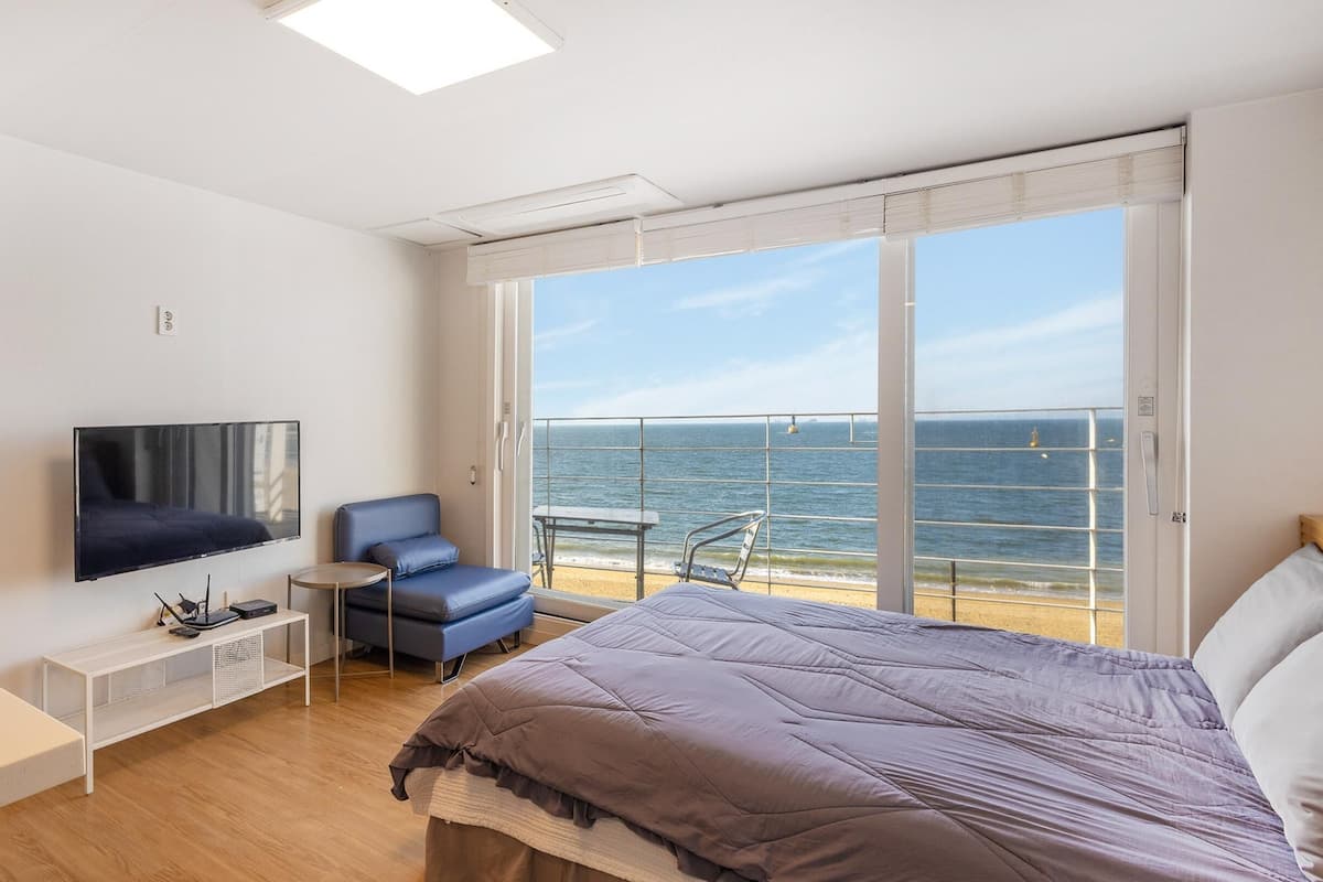 Ein modernes Hotelzimmer mit Bett, Fernseher, Schreibtisch und einem Balkon mit Meerblick.