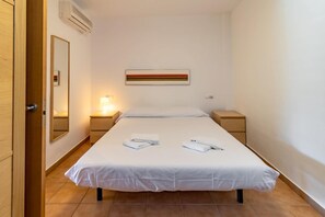 Hotellihuone, jossa on sänky, kaksi yöpöytää, seinälle asennettu ilmastointilaite, kehystetty taideteos ja puinen ovi.