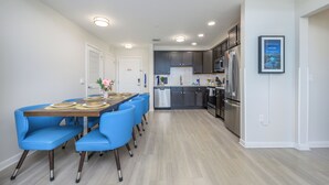 Una cocina moderna con armarios oscuros, electrodomésticos de acero inoxidable y una zona de comedor con sillas azules y una mesa de madera.