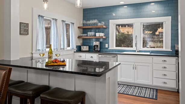 A modern kitchen with a central island, white cabinetry, blue backsplash, and pendant lighting. - Maple Haus Entire Property | Sleeps 18 | Great Location (Fredericksburg)