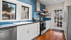 Une cuisine avec des meubles blancs, un évier en acier inoxydable, une cuisinière et un réfrigérateur.