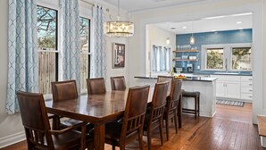 Un coin repas avec une table et des chaises en bois, un lustre et une vue sur la cuisine.