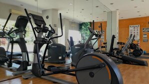 Un gimnasio con diverso equipo de ejercicio, incluyendo cintas de correr y bicicletas estáticas, y un espejo grande en la pared.