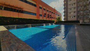 Una piscina con borde de azulejos, rodeada por un camino de ladrillo y edificios cercanos.