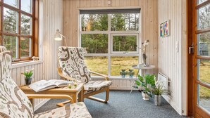 Una habitación acogedora con paredes de madera y ventanas amplias, que incluye dos sillas, una mesita y una planta en maceta.