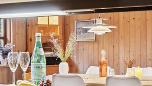 Un comedor con paredes de madera, una mesa dispuesta con una botella de S.PELLEC, copas y una bandeja de frutas.