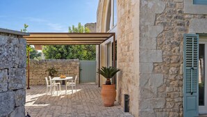 A stone building with a covered patio, a table with chairs, and a potted plant. - Villa Pruno, Scicli, Italy (Scicli)