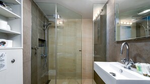 A modern bathroom with a glass-enclosed shower, a white sink with a chrome faucet, and a mirror above the sink.