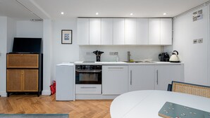 A compact kitchen with white cabinets, a built-in oven, a dishwasher, and a small countertop with a kettle and utensils.