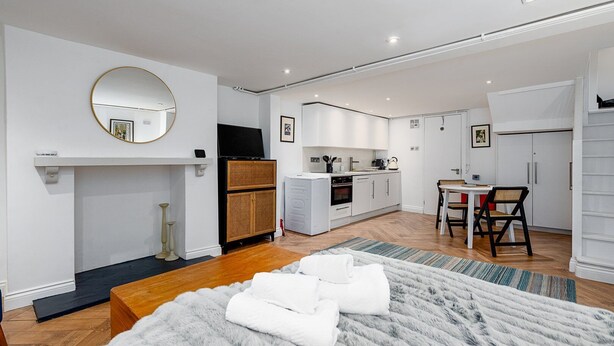 A modern bedroom with a large bed, a fireplace, and a kitchen in the background.