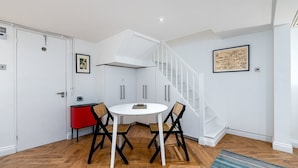 A compact room with a white table and chairs, a red cabinet, and a staircase.
