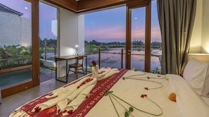 Ein Hotelzimmer mit einem großen Bett, einem Schreibtisch und Blick auf ein Gewässer und Grünflächen.
