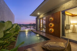 A modern outdoor pool area with a wooden deck, a lounge chair, and a view of the surrounding landscape. - Villa Subak II (Ubud)