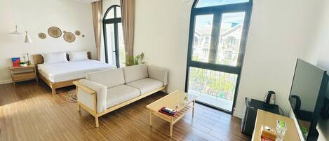 Una habitación de hotel moderna con cama, sofá, piso de madera, ventanas grandes y televisión.