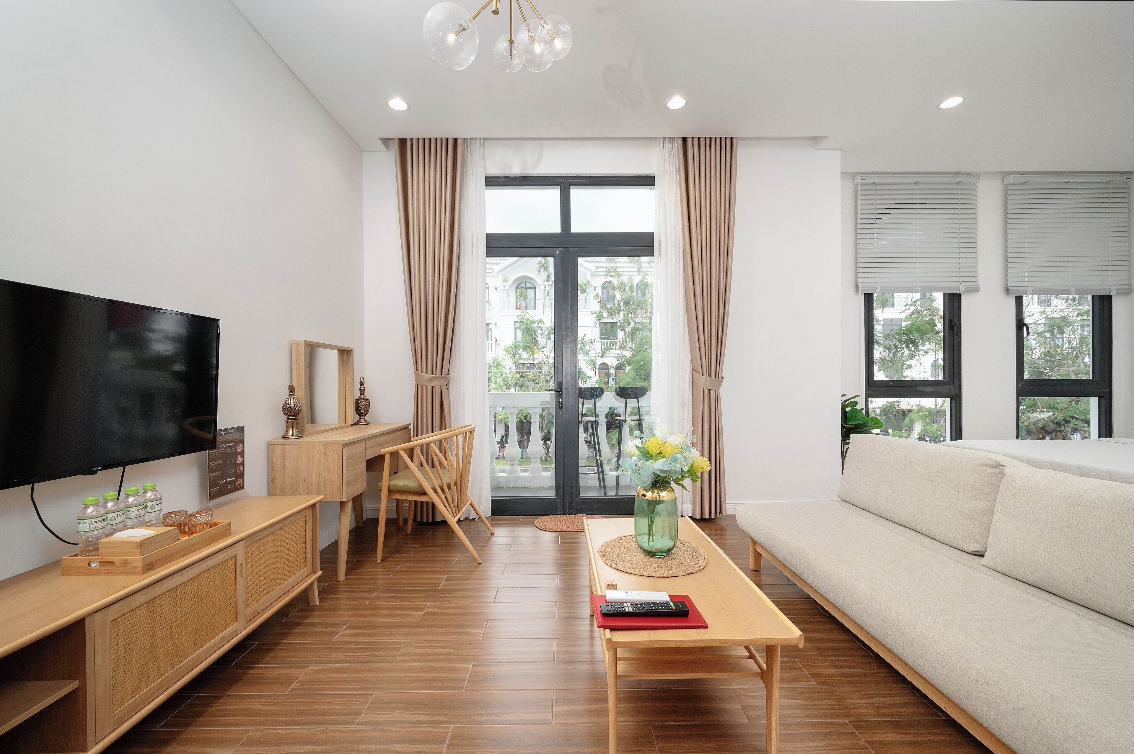 A modern living room with a flat-screen TV, wooden furniture, a sofa, and a view through a glass door.