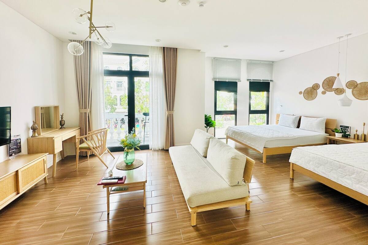 A modern hotel room with a wooden floor, a sofa, a bed, a desk, and a balcony with curtains.