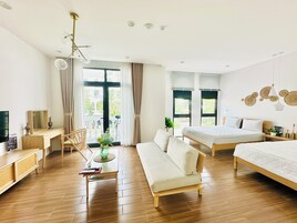 Una habitación de hotel moderna con suelo de madera, un sofá, una cama, un escritorio y un balcón con cortinas.