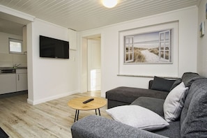 A modern living room with a grey sofa, a wooden coffee table, and a flat-screen TV mounted on the wall.