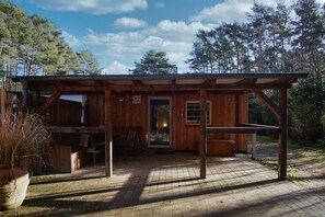 Un rustico chalet in legno con veranda coperta, zona pranzo con sedie e un'ampia finestra.