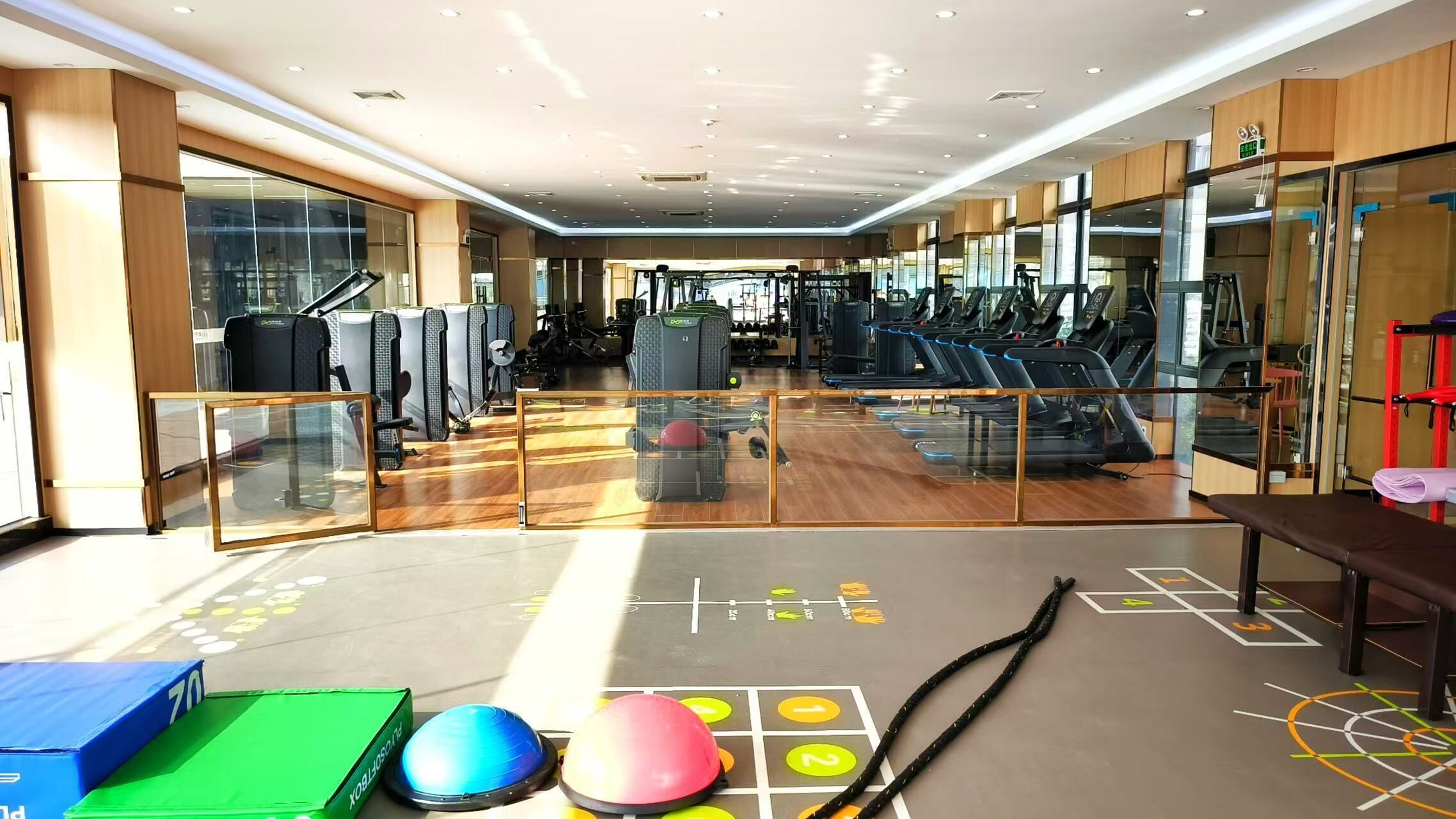 Un gimnasio moderno con equipo de ejercicio, suelo de madera y divisiones de vidrio.
