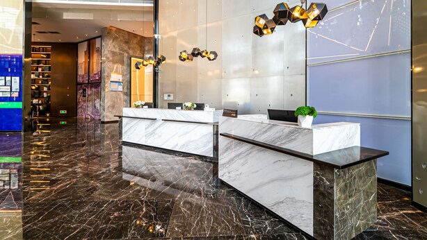 A modern reception desk with marble countertops and a black base, surrounded by a polished marble floor.