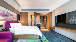A modern hotel room with a large bed, a flat-screen TV, a seating area, and a cityscape artwork on the wall.