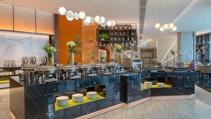 A modern hotel lobby with a marble reception desk, buffet area, and seating.