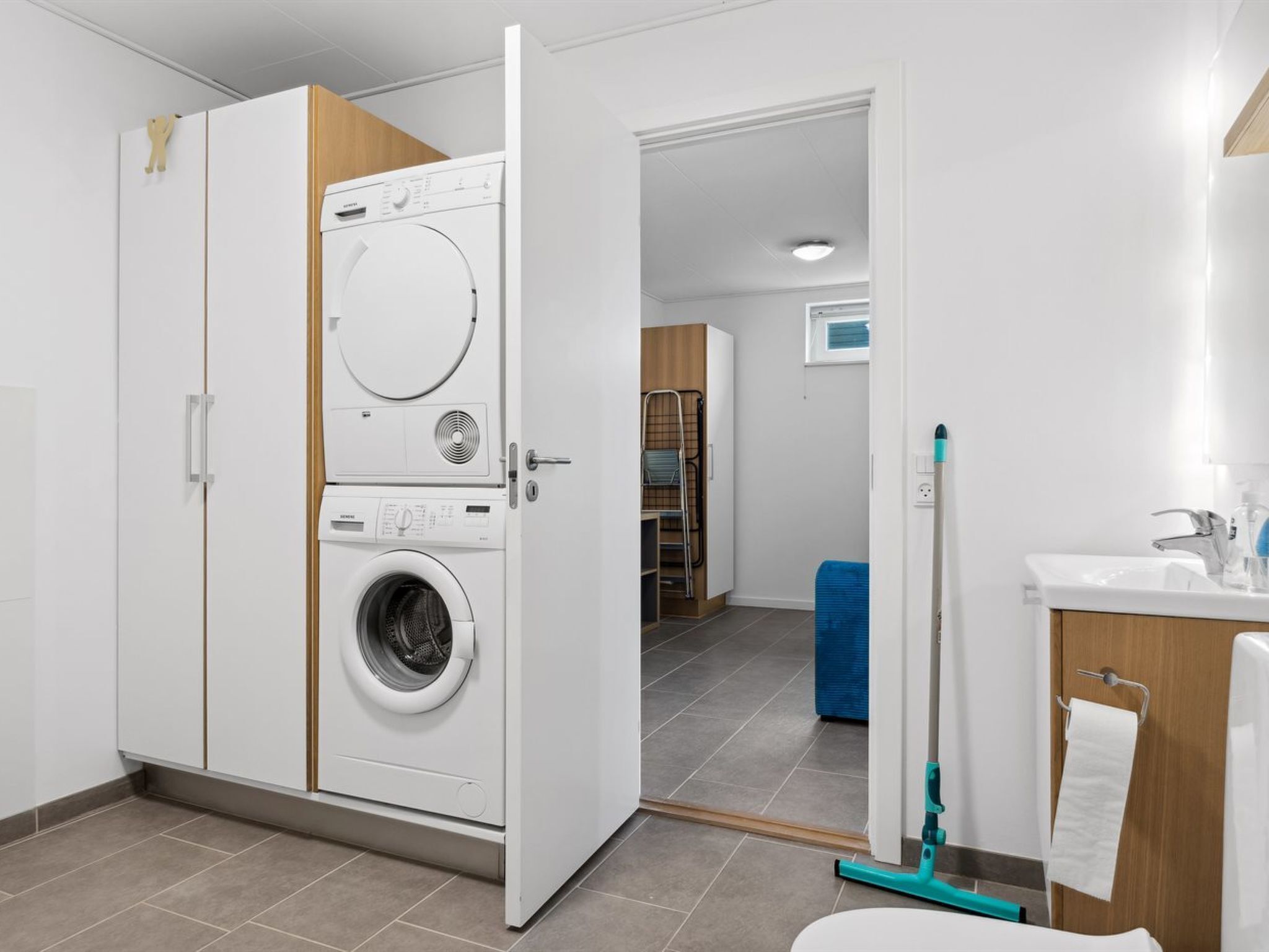 Une buanderie équipée d’un lave-linge et d’un sèche-linge à chargement frontal, d’une serpillière bleue, et une salle de bain avec un lavabo et un porte-serviettes.