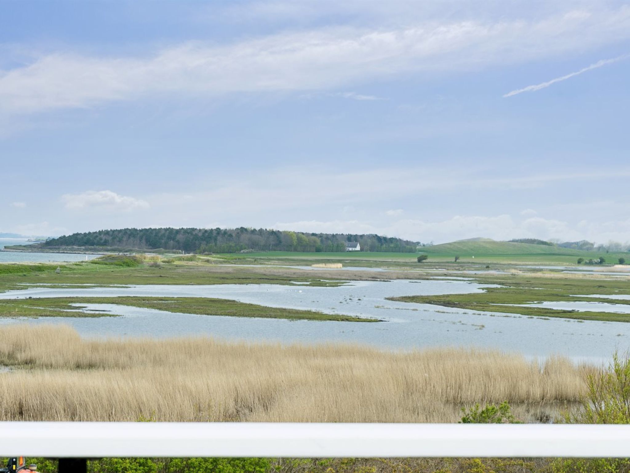 Un paysage plat avec une étendue d’eau, des zones herbeuses et, au loin, une colline sur laquelle se trouve un bâtiment.