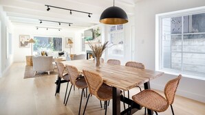 A spacious dining area with a wooden table and wicker chairs, a pendant light, and a large window providing natural light. - Secluded Downtown Modern Lux Retreat in Redwoods (Mill Valley)