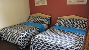 A room with two beds, each with patterned bedding and a blue blanket. There are two framed pictures on the wall. - ECONOMY INN (Santa Maria)